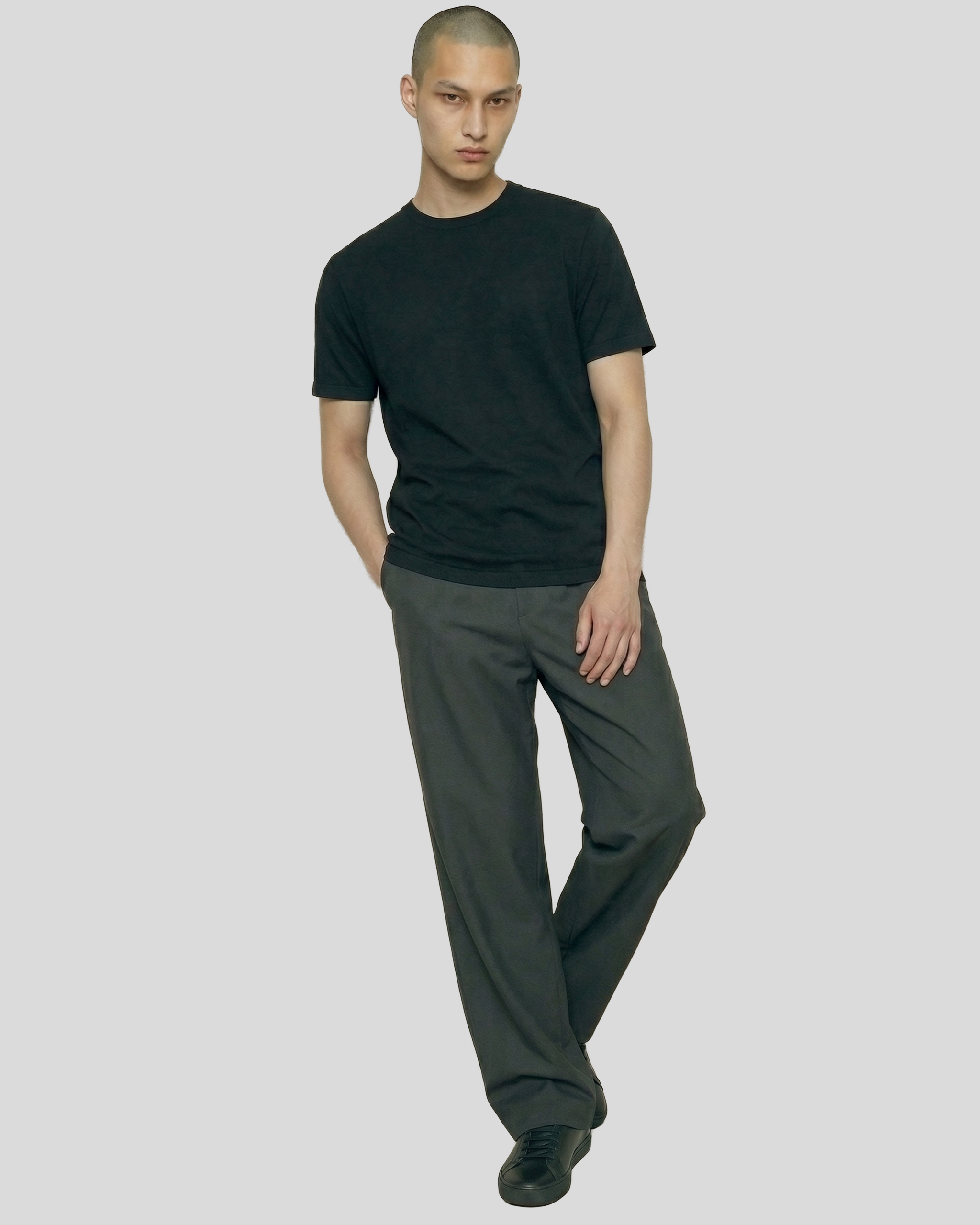 Man wearing a black t-shirt and gray pants on a plain background
